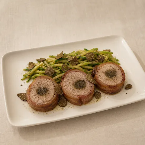 Pancetta-wrapped pork fillets with courgettes and fresh truffle on a rectangular plate.