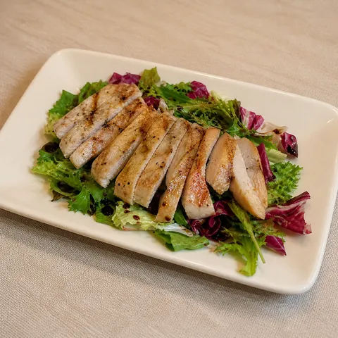 Turkey tagliata on mixed leaves with balsamic, served on a rectangular plate.