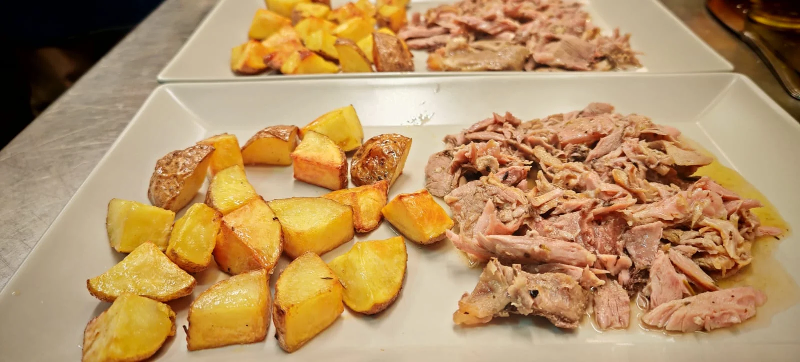 Shredded roast of the day with roast potatoes on a rectangular white platter.