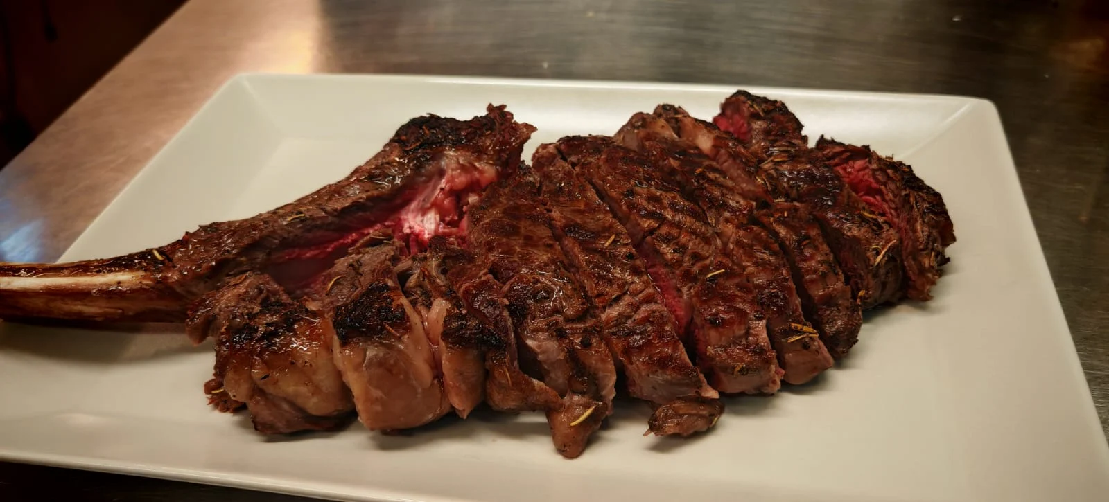 Cooked and sliced beef tomahawk served on a large rectangular white platter.